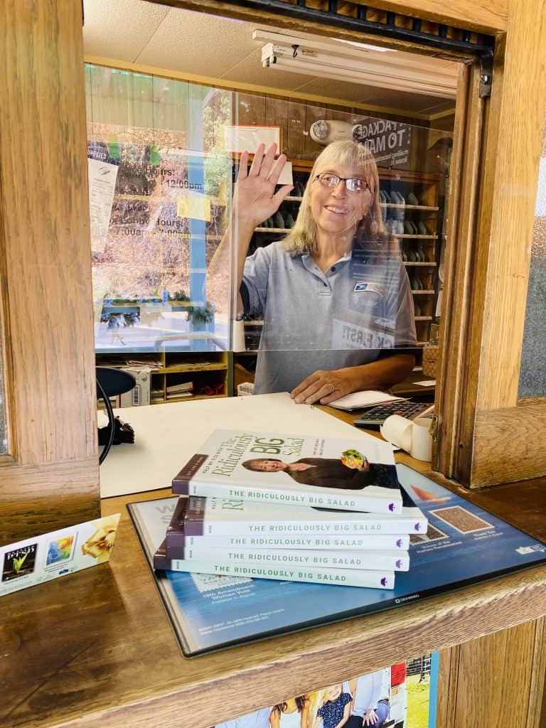 Postmaster Sandy waving from inside the post office