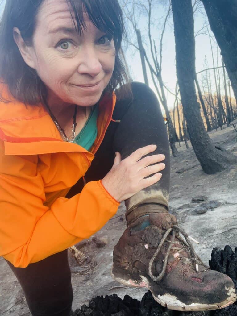 Amanda with shoes covered in mud and ash in a burned forest