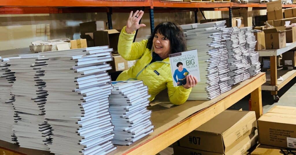 Amanda Rose with stacks of signed books, waving